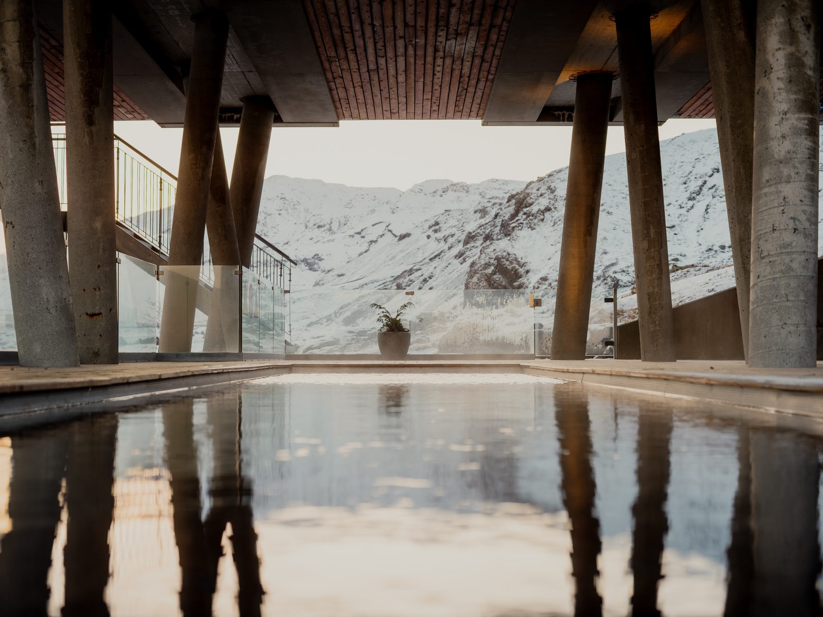 Upphituð sundlaug undir steinsúlum með snævi þökt fjall